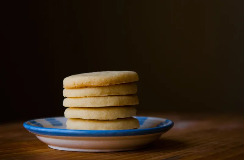 Ein Stapel aus fünf runden, hellen Butterplätzchen liegt auf einem blau-weiß gestreiften Teller.