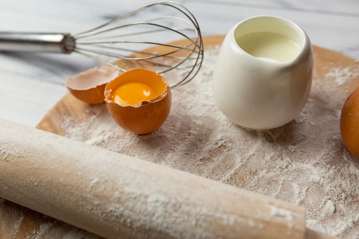 Zutaten wie Mehl, Eier und Milch auf einer Küchenarbeitsplatte