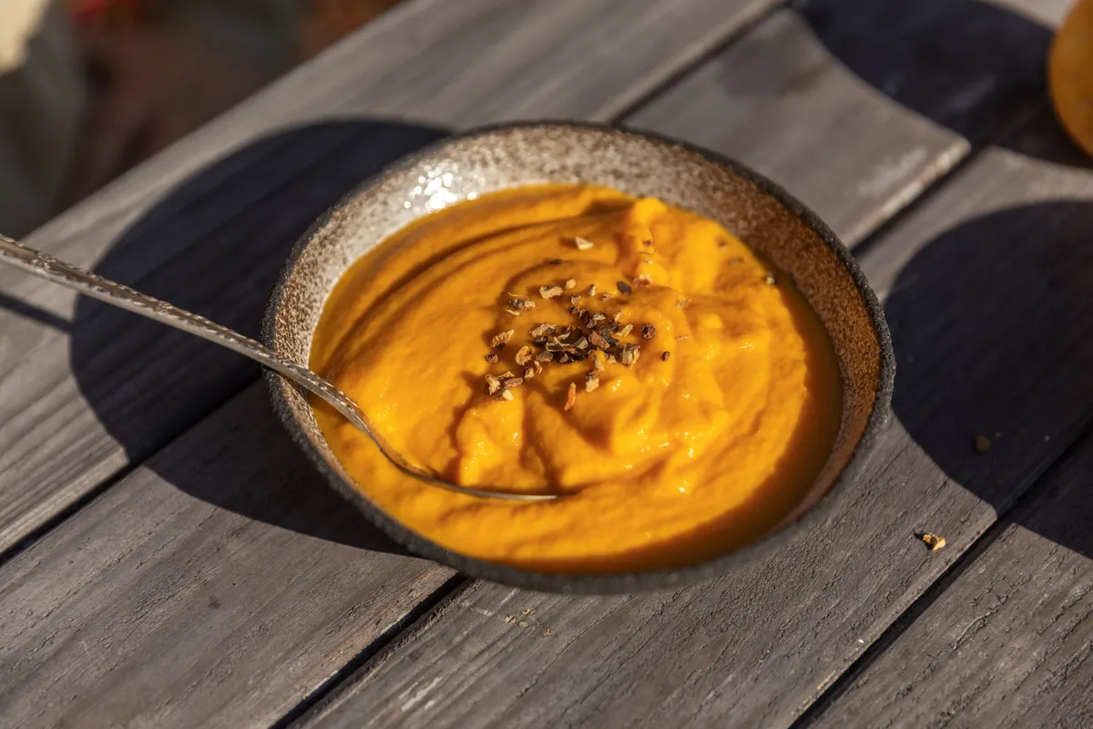 Eine Schüssel cremiger Kürbissuppe, garniert mit Kernen und frischen Kräutern.