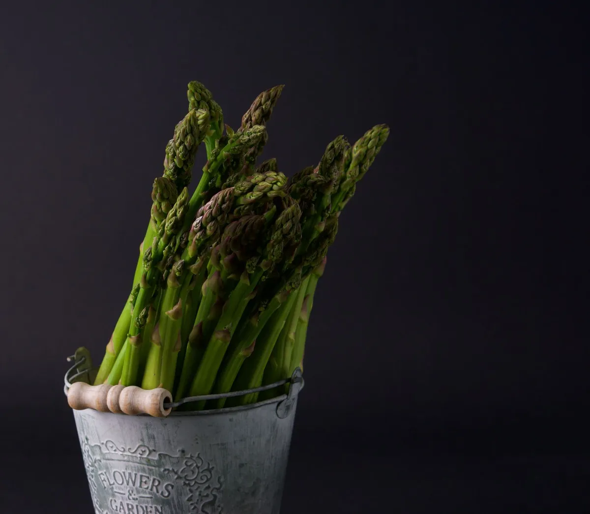 Ein Bund frisch geernteter grüner Spargel liegt neben einem Sparschäler auf einem Brett.