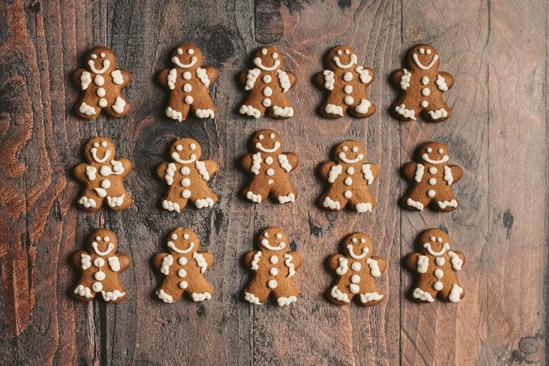 Frisch gebackene Lebkuchenmännchen mit weißer Zuckergussverzierung liegen auf einem dunklen Holztisch.